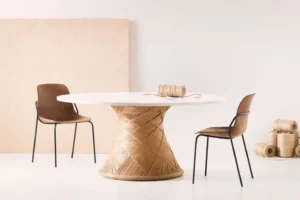 Ronde tafel met een opvallend onderstel van geweven touw, gecombineerd met twee stoelen met een zitting van donkerbruin, natuurlijk materiaal en een zwart stalen frame. De rustige setting benadrukt de focus op biobased en circulair design.